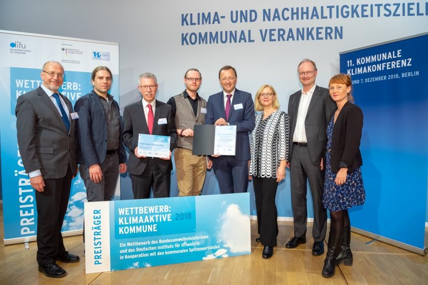Bild Quelle: SK:KK/difu  Die Delegation aus Bad Ems (Verwaltungsspitze, Fachplaner, Klimaschutzmanagement) freuen sich über den Preis als Klimaaktive Kommune 2018 – übergeben durch Vertreter der kommunalen Spitzenverbände und Umweltministerin Svenja Schulze