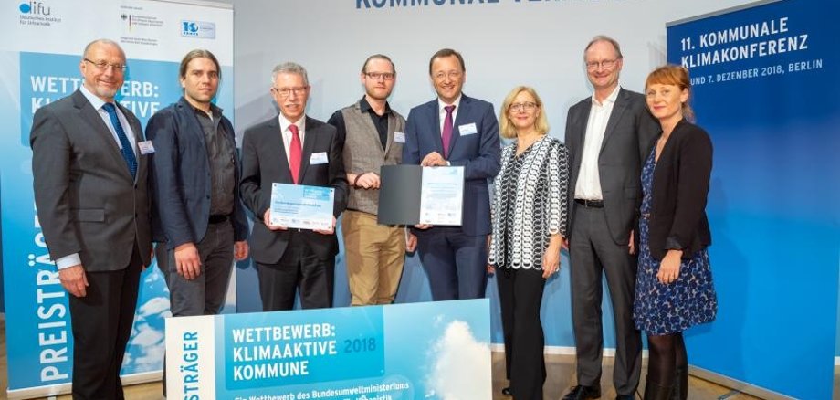 Bild Quelle: SK:KK/difu  Die Delegation aus Bad Ems (Verwaltungsspitze, Fachplaner, Klimaschutzmanagement) freuen sich über den Preis als Klimaaktive Kommune 2018 – übergeben durch Vertreter der kommunalen Spitzenverbände und Umweltministerin Svenja Schulze